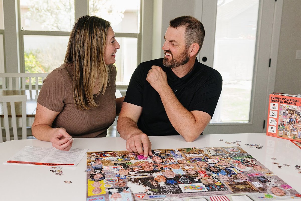 A couple laughing together at the table while building the Funny Political Quotes 1,000-piece puzzle, which collects 72 funny quotes from politicians and first ladies