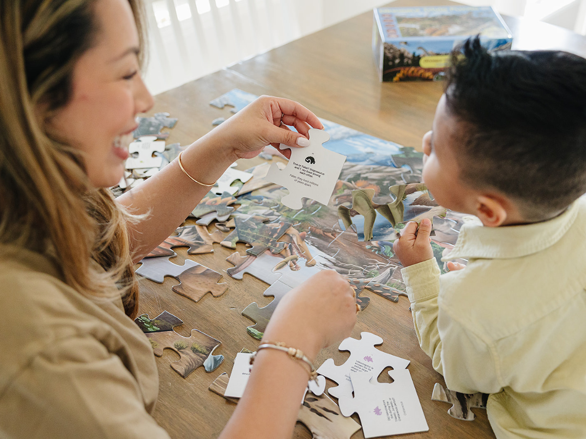 Mom and son doing a large-piece dinosaur puzzle, and reading the dinosaur trivia from the backs of the puzzles pieces