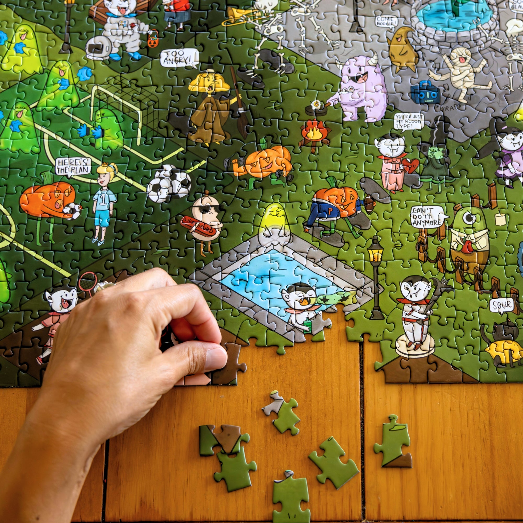 Person assembling 1,000 piece Halloween Joke Puzzle with illustrated Halloween characters on a wooden table