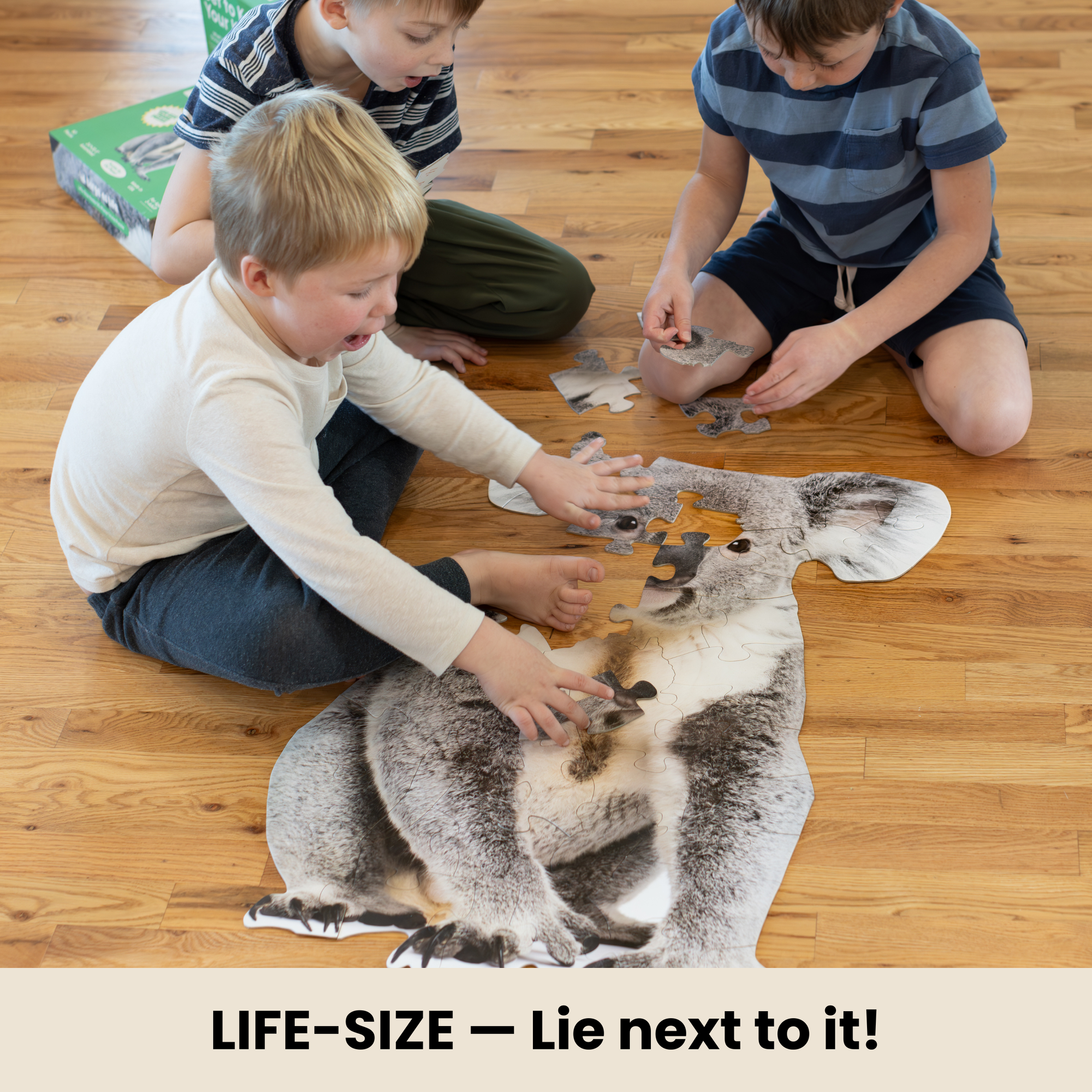 Three children playing with a large koala-shaped puzzle on a wooden floor.