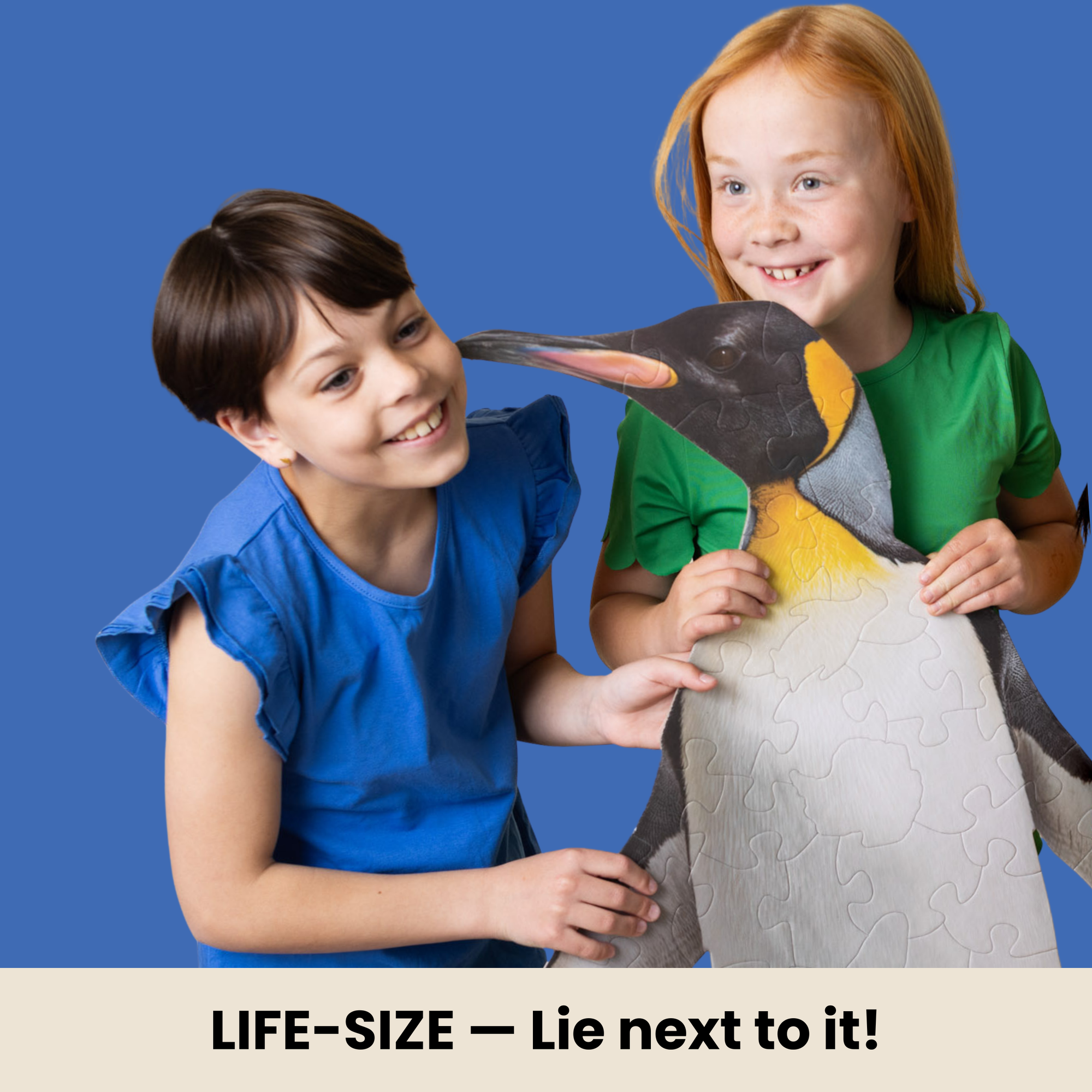 Two children holding a large life-size penguin puzzle against a blue background.